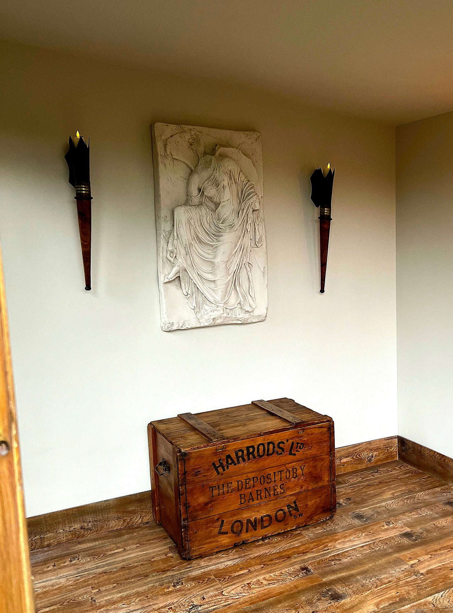 A marble relief sculpture plaque depicting Nike, the goddess of victory, hanging on a wall above a wooden chest.