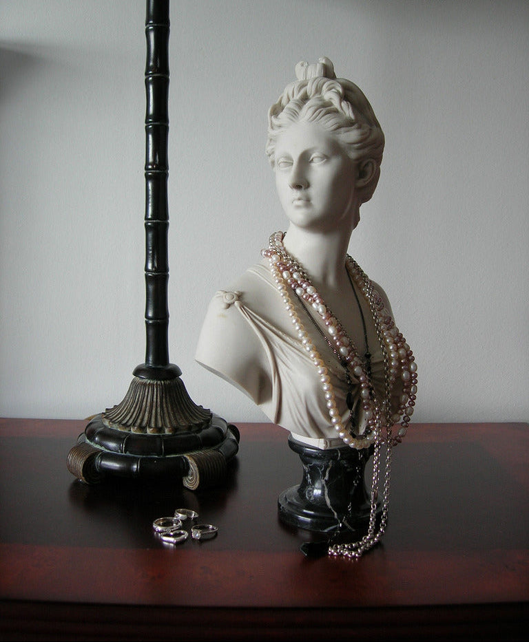 Bust of a woman with pearls draped over it on a wooden surface next to a lamp.