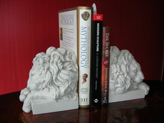 A pair of white marble bookends in the shape of lions' heads, with books stacked on top of them.