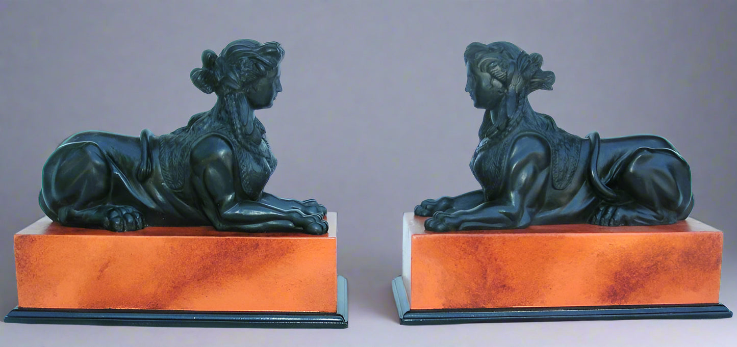 A pair of decorative sphinx sculptures finished in basalt black with a sienna base, positioned on wooden plinths.