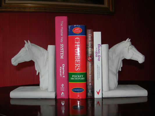 A pair of white bookends in the shape of horses' heads, with books placed between them on a dark surface against a red background.